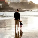 Fotografía de padre e hija caminando en la playa que representa vínculo familiar, acompañamiento emocional y conexión humana